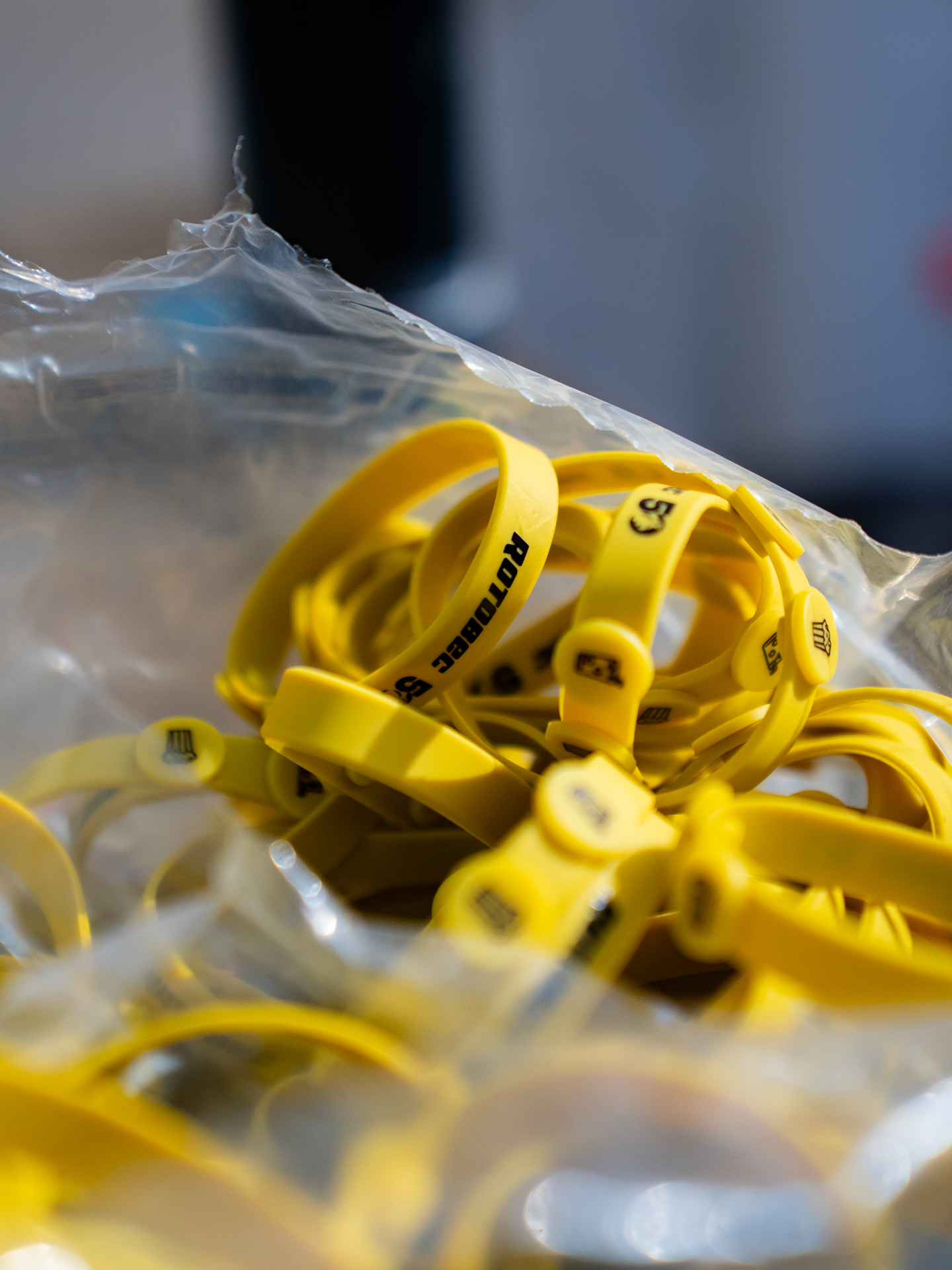 Gros plan sur plusieurs bracelets jaunes avec un texte noir, empilés dans un sac en plastique transparent. L'arrière-plan est flou.